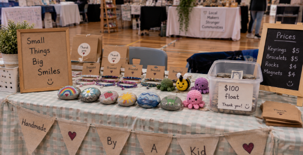 A child's market stall with handmade items, a handwritten sign and a container of coins