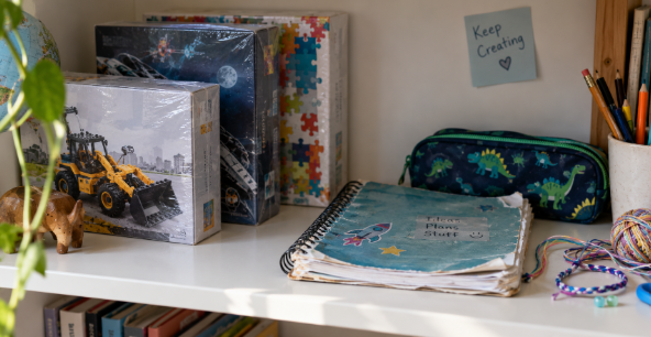 A child's shelf with unopened boxed gifts at the back and a well-used notebook at the front 